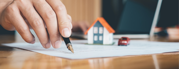 a small image of person's hand with pen...signing document with small house on top